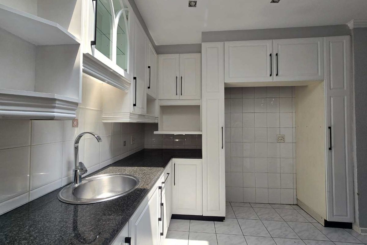 A clean, modern kitchen featuring white cabinetry, dark granite countertops, a stainless steel sink, and tiled finishes throughout.