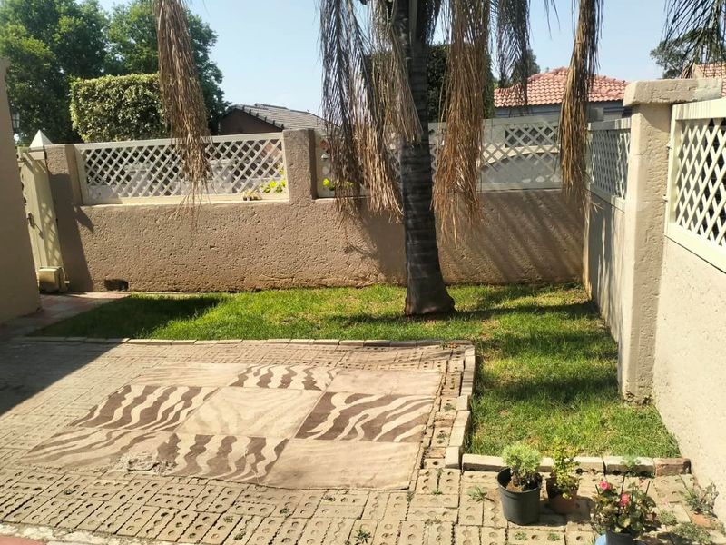 A private rear garden featuring a paved patio area, established lawn, and perimeter boundary walls with decorative lattice fencing.