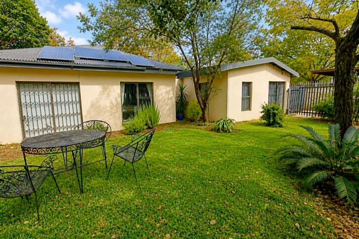 A well-maintained rear garden featuring a lush lawn, mature trees, and a house exterior equipped with solar panels and secure sliding door access.