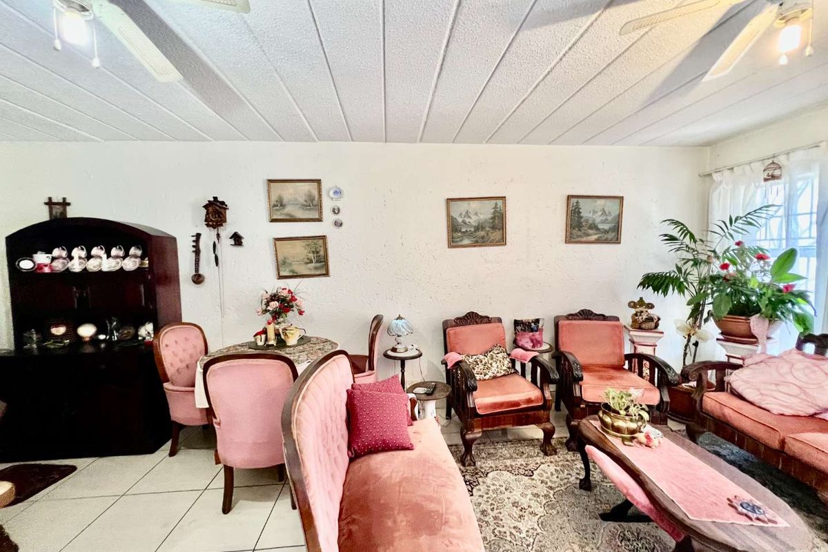 A spacious living area featuring tiled flooring, dual ceiling fans, and textured wall finishes, providing a functional and traditional living space.