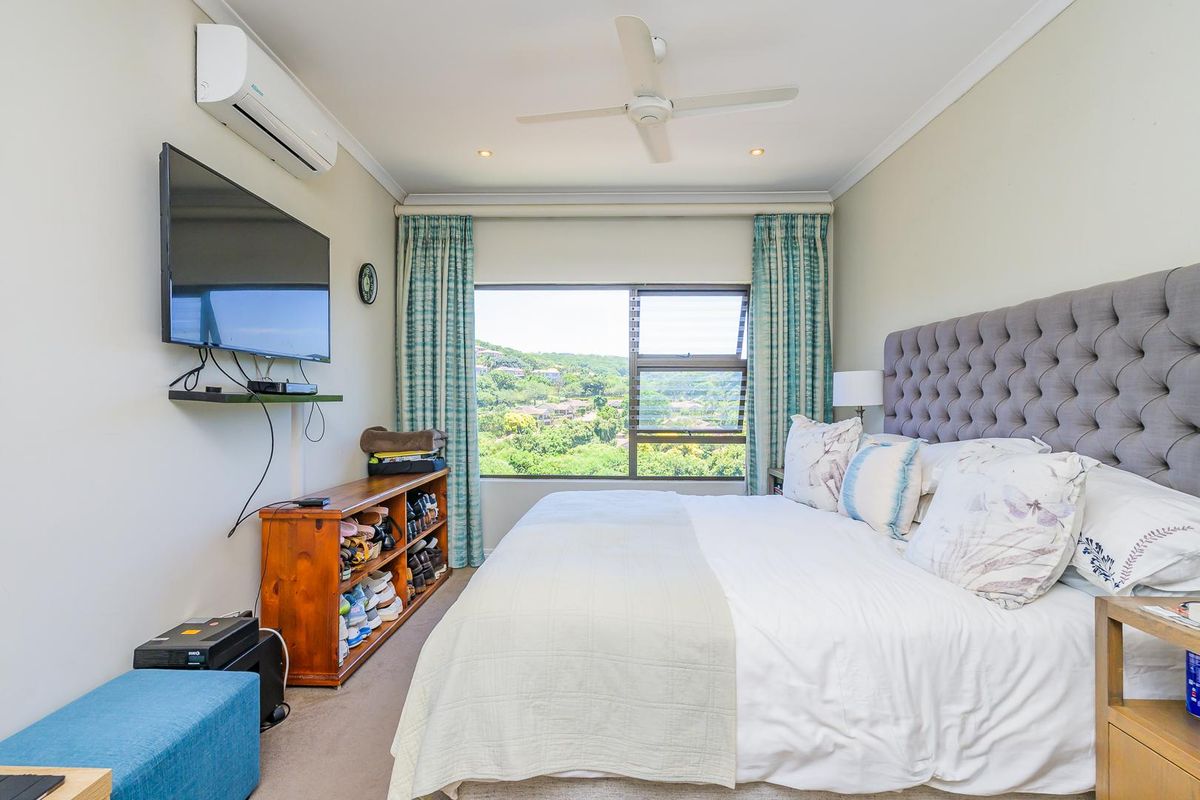 A well-lit bedroom featuring a ceiling fan, wall-mounted air conditioning unit, and a large window offering scenic hillside views.