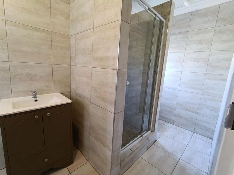 A clean, modern bathroom featuring a vanity cabinet with basin and a glass-enclosed shower with neutral wall and floor tiling.