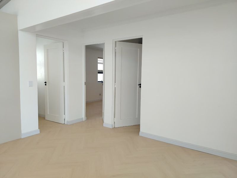 A bright, empty hallway featuring modern light-toned herringbone flooring and clean white interior doors leading to adjacent rooms.