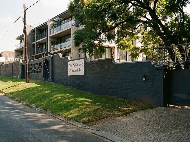 Street view of The Solomon apartment complex, featuring a secure perimeter wall, electric fencing, and paved driveway access.