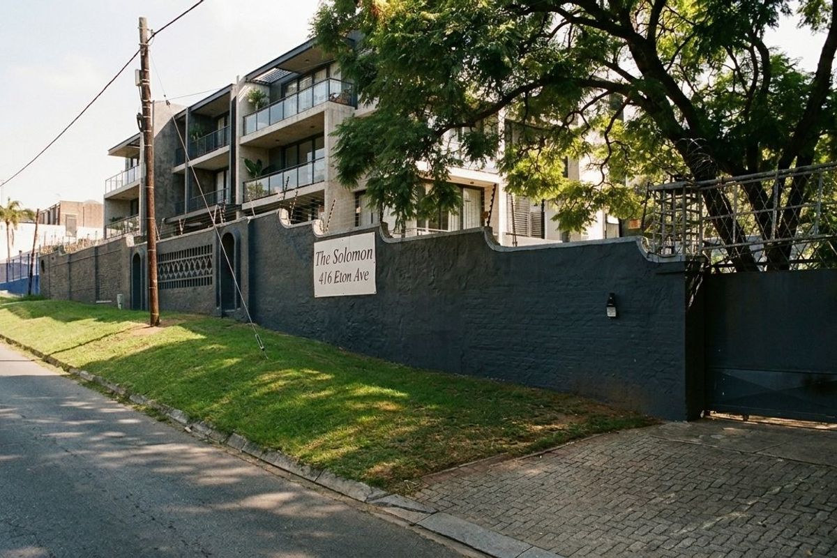 Street view of The Solomon apartment complex, featuring a secure perimeter wall, electric fencing, and paved driveway access.