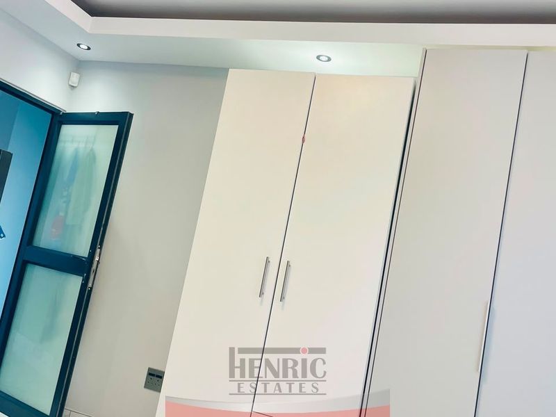 A bedroom featuring modern white built-in cupboards, recessed ceiling lighting, and a contemporary cove ceiling design.