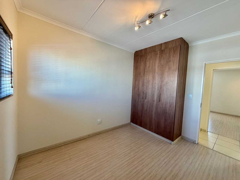 A clean, empty bedroom featuring wood-look laminate flooring, neutral walls, and dark wood-finish built-in cupboards.