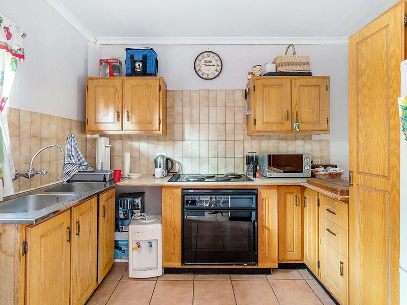 A functional kitchen featuring wooden cabinetry, laminate countertops, a built-in oven with electric hob, and tiled backsplash and flooring.