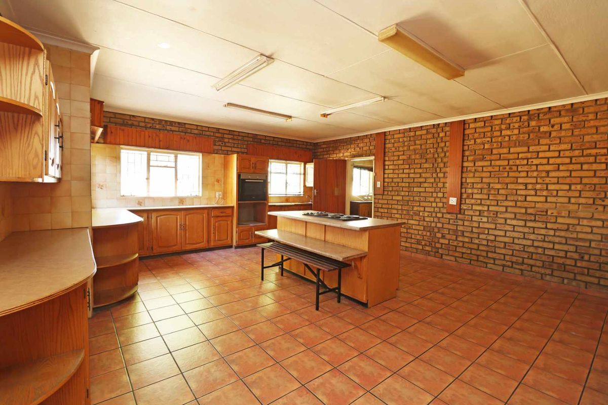 Spacious kitchen featuring exposed brick walls, tiled flooring, built-in wooden cabinetry, and a central island with a built-in hob and oven.