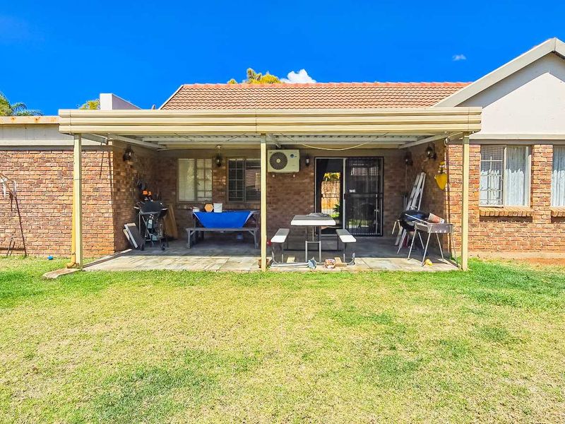 Rear view of the townhouse featuring a covered patio area, brick exterior, and a spacious garden.