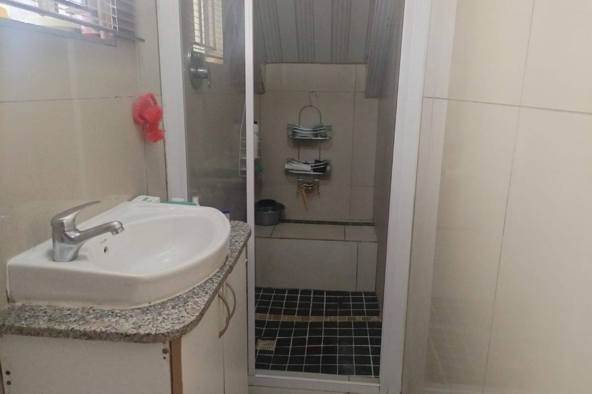 A functional bathroom featuring a vanity basin with a mixer tap and a separate shower enclosure with tiled finishes.