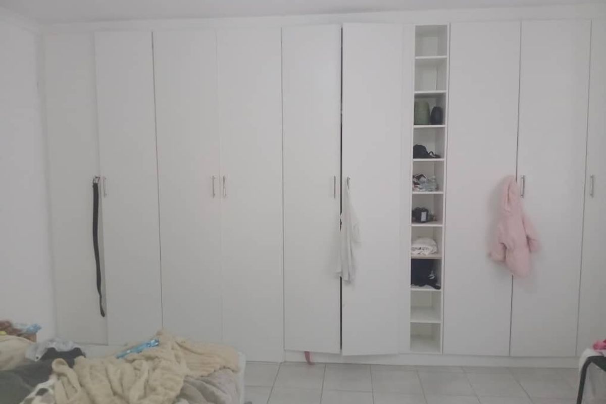 A bedroom featuring extensive floor-to-ceiling built-in white cabinetry with integrated shelving and modern hardware.