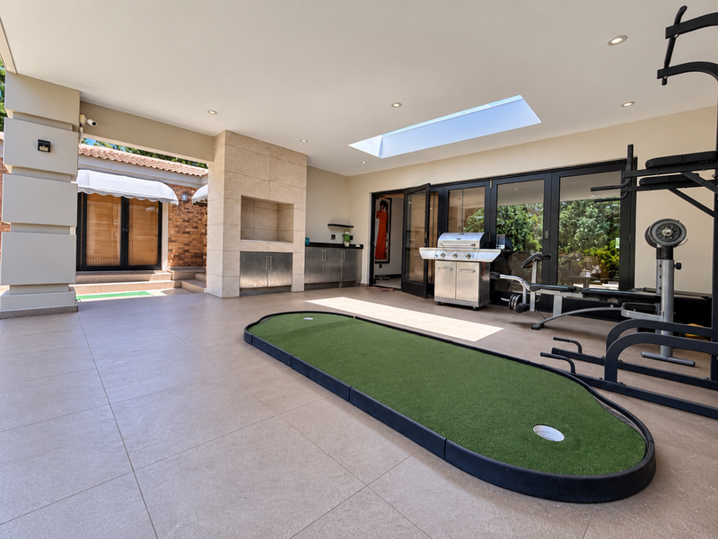 Spacious covered patio featuring a built-in braai, stainless steel cabinetry, skylight, and large aluminium sliding doors leading to the garden.