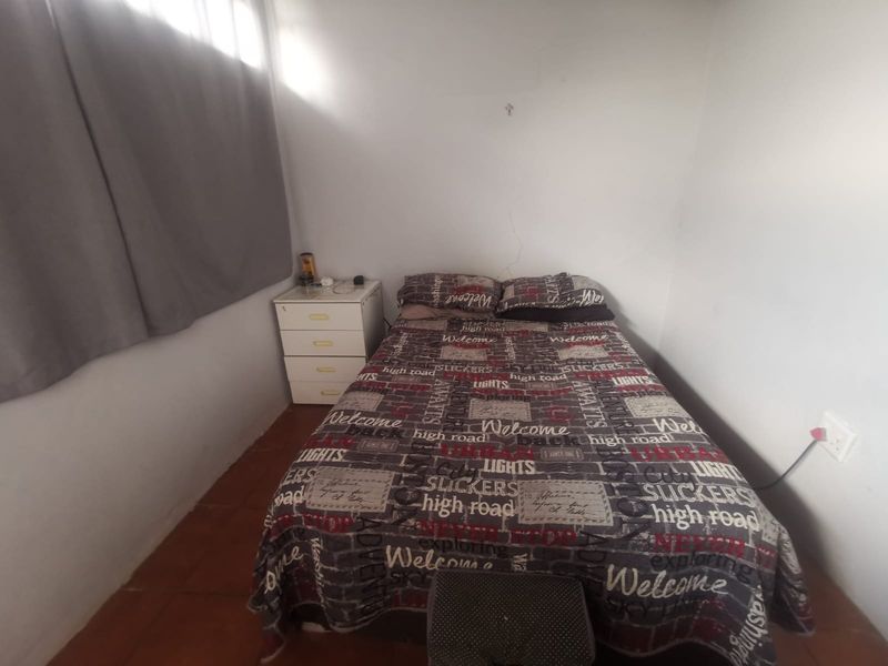 A compact bedroom featuring tiled flooring and plain walls, currently requiring minor maintenance to address visible wall cracking.