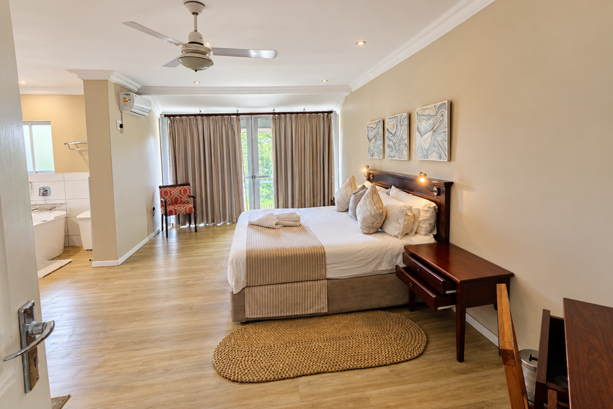 Spacious bedroom featuring laminate flooring, crown molding, recessed lighting, and an integrated air conditioning unit, with direct access to a balcony through sliding glass doors.