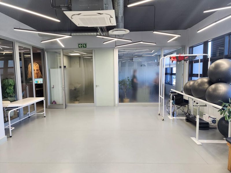 A modern, well-lit office gym space featuring glass partitions, industrial-style exposed ceiling elements, and durable vinyl flooring.