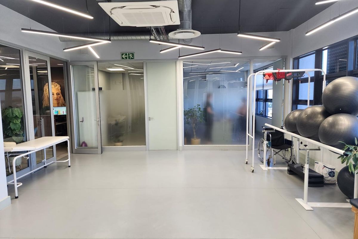 A modern, well-lit office gym space featuring glass partitions, industrial-style exposed ceiling elements, and durable vinyl flooring.