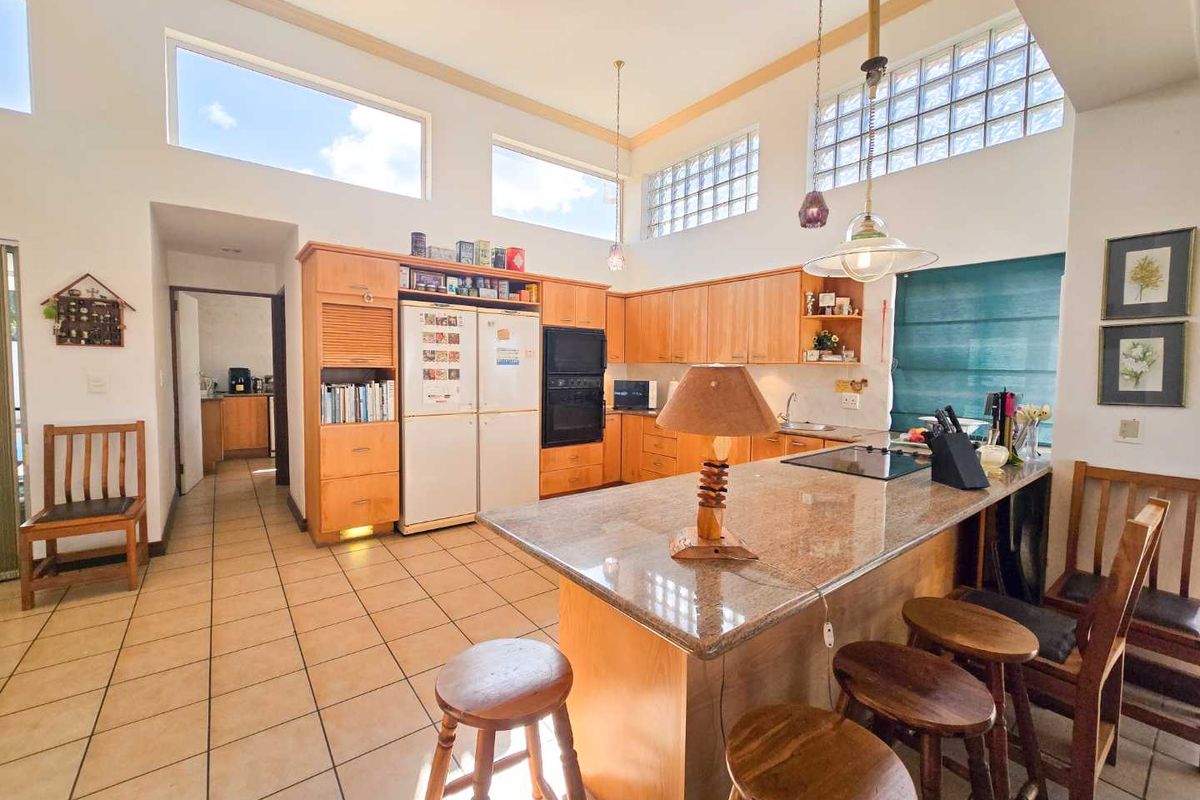 Spacious kitchen featuring light wood cabinetry, granite countertops, a central island with breakfast bar, and high-level windows providing natural light.
