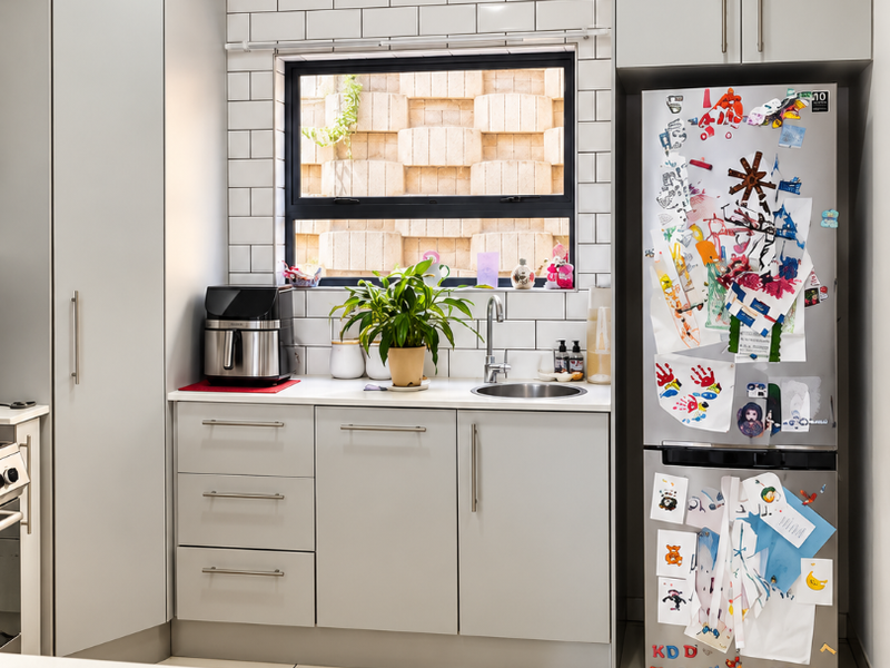 A modern, well-maintained scullery featuring light grey cabinetry, subway tile backsplash, stainless steel sink, and large format floor tiles.