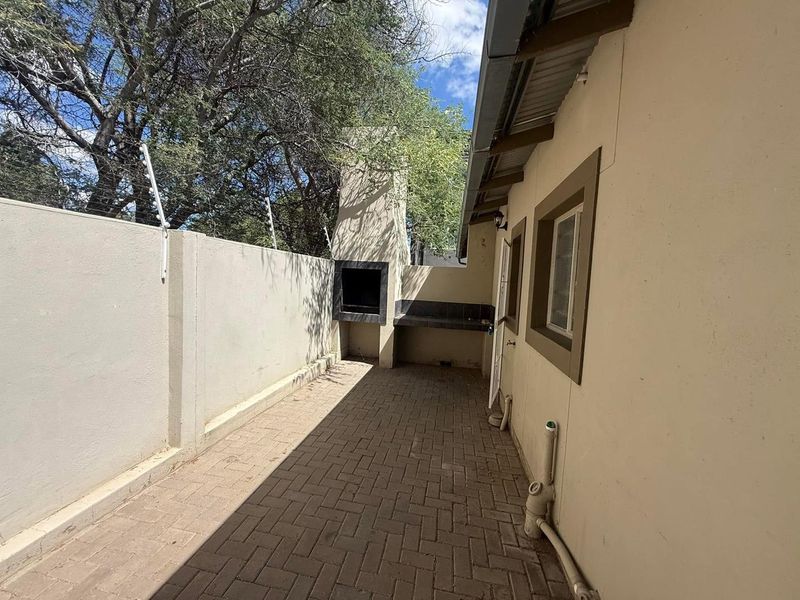 A paved outdoor patio area featuring a built-in braai, enclosed by a boundary wall with electric fencing.