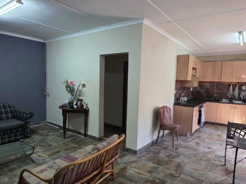 Open-plan living and kitchen area featuring tiled flooring, built-in cabinetry, and security window bars, offering a functional layout with potential for modernization.