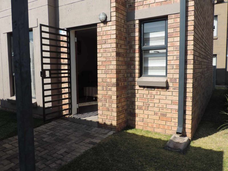 Front entrance of a townhouse featuring face brick exterior, a paved walkway, and a secure metal gate.