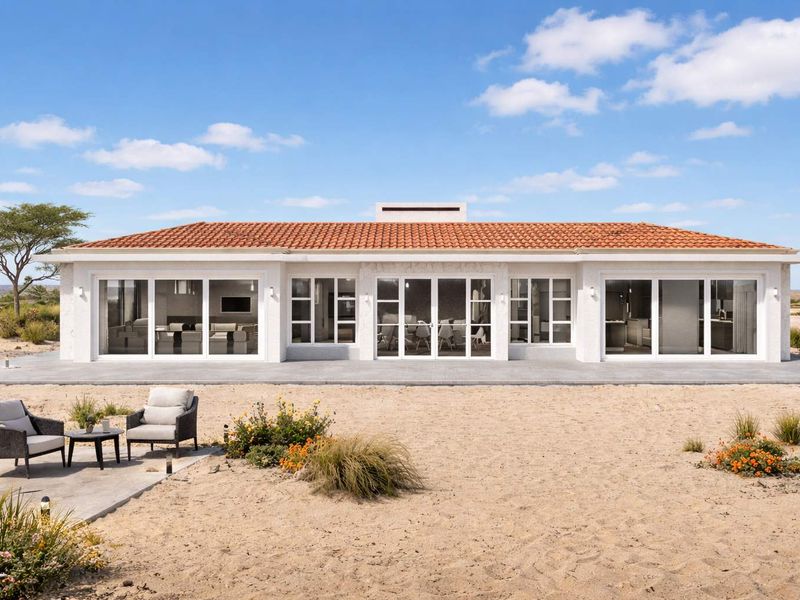 Rear view of a modern single-story home featuring a terracotta tiled roof, white stucco exterior, and extensive glass sliding doors opening onto a concrete patio.