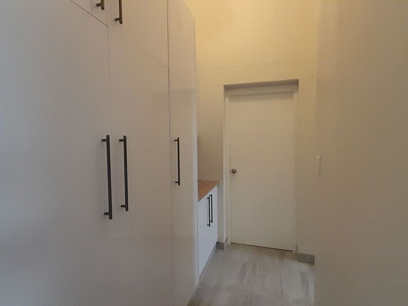 A clean, minimalist hallway featuring extensive built-in white cabinetry with modern dark hardware and light-toned flooring.