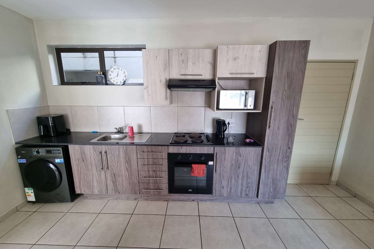 Compact kitchen featuring wood-grain cabinetry, dark granite countertops, built-in oven, hob, extractor fan, and tiled flooring.