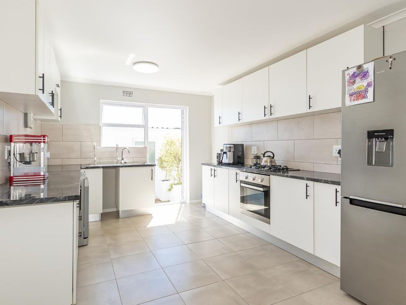 Modern kitchen featuring white cabinetry, stone-look countertops, stainless steel oven, gas hob, and tiled flooring with direct access to the outdoor area.