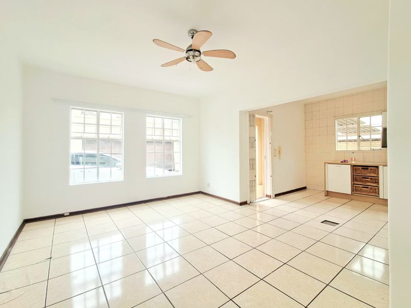 Spacious open-plan living area featuring neutral tiled flooring, a ceiling fan, and an adjoining kitchen space with built-in cabinetry and tiled splashback.