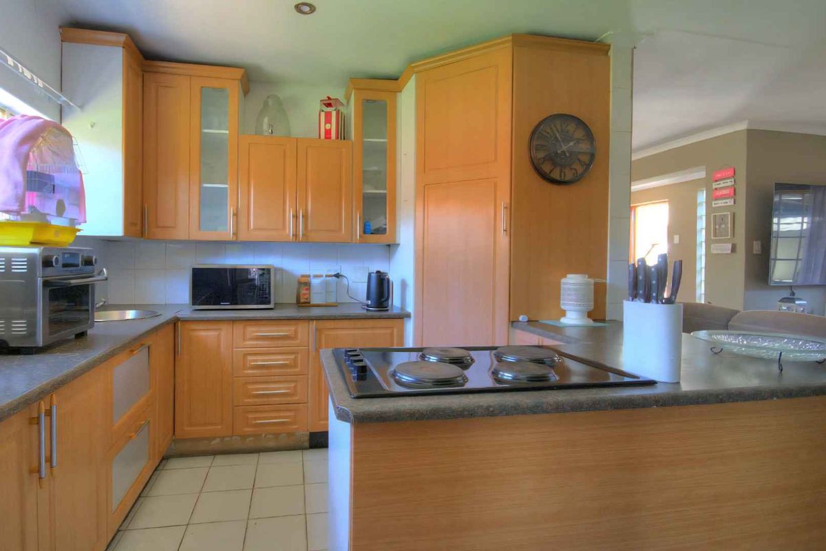 A functional kitchen featuring light wood cabinetry, a built-in electric hob, and tiled flooring, seamlessly connecting to the adjacent living area.