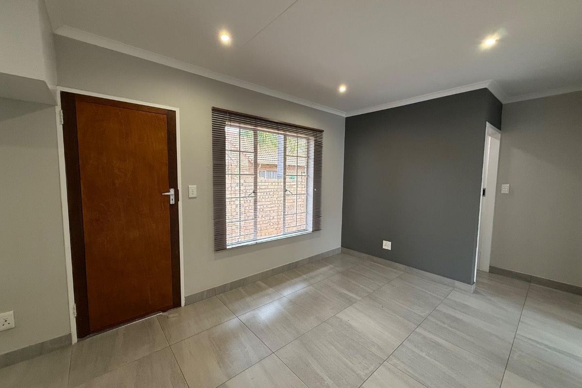 A bright, empty bedroom featuring neutral tiled flooring, recessed ceiling lighting, and a contrasting dark grey feature wall.