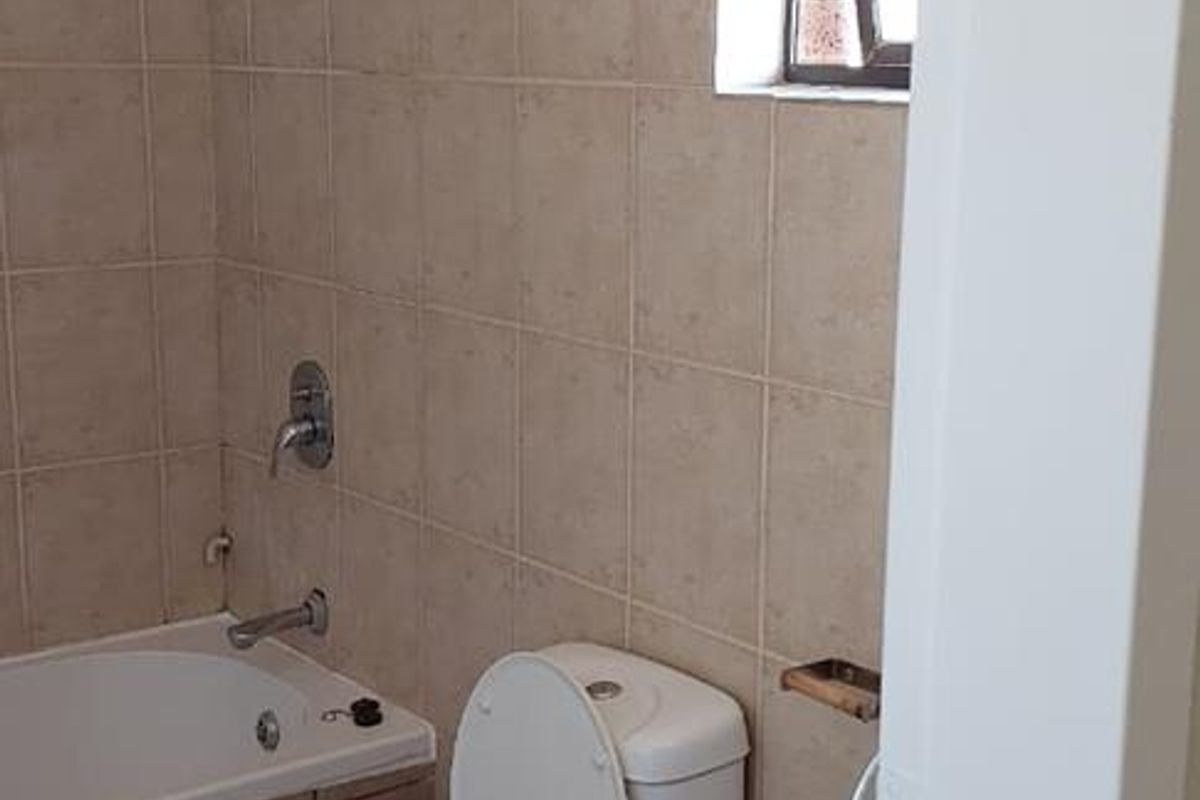 A compact bathroom featuring a bathtub with shower head, pedestal basin, and toilet, finished with neutral wall and floor tiles.