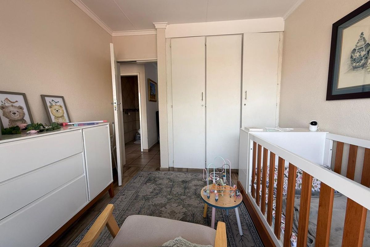 A functional bedroom featuring built-in cupboards, tiled flooring, and classic cornicing, providing a practical space with direct access to an adjacent room.