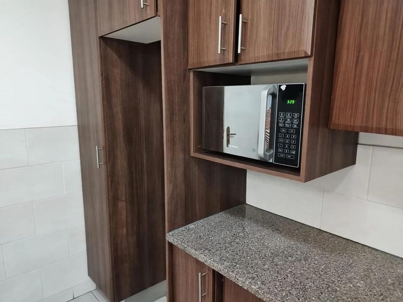 A modern kitchen area featuring dark wood cabinetry, granite countertops, a built-in microwave, and a clean tiled backsplash.