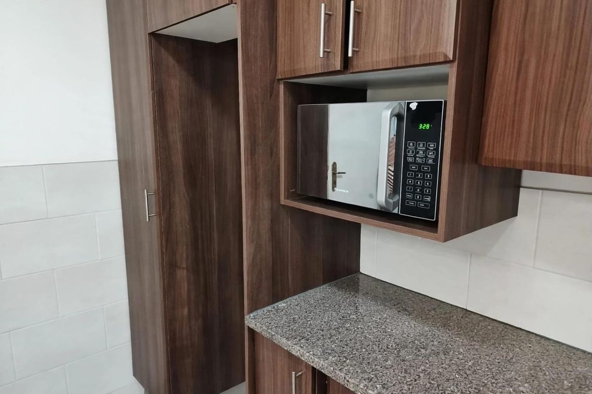 A modern kitchen area featuring dark wood cabinetry, granite countertops, a built-in microwave, and a clean tiled backsplash.
