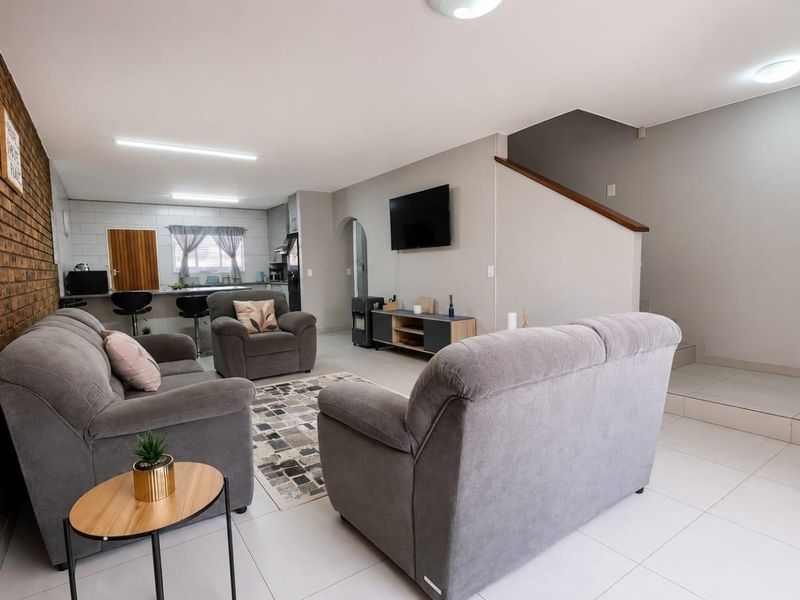 Spacious open-plan living area featuring an exposed brick wall, tiled flooring, and a staircase, seamlessly connecting to the kitchen space.
