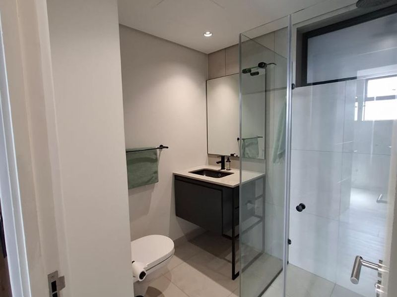 Modern bathroom featuring a wall-mounted vanity with integrated basin, black tapware, wall-hung toilet, and a spacious glass-enclosed shower with a rain shower head.