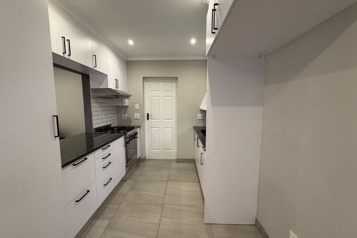 Modern galley-style kitchen featuring white cabinetry, dark granite countertops, tiled flooring, and a built-in gas stove with extractor fan.