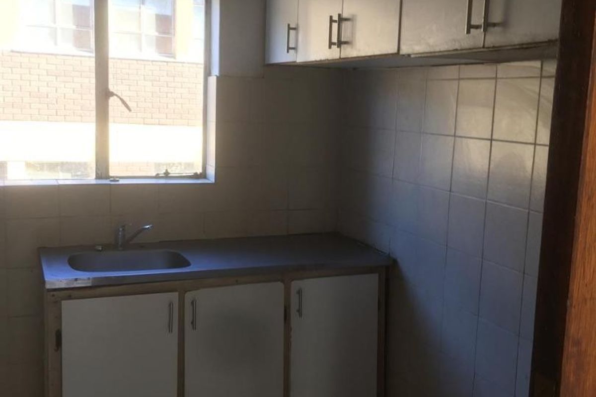 A compact, dated kitchen featuring built-in cabinetry, a stainless steel sink, and tiled finishes, offering potential for a modern renovation.