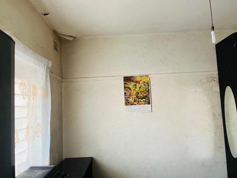 A bedroom interior showing signs of significant wear, including peeling ceiling paint and water damage on the walls, requiring maintenance and cosmetic updates.