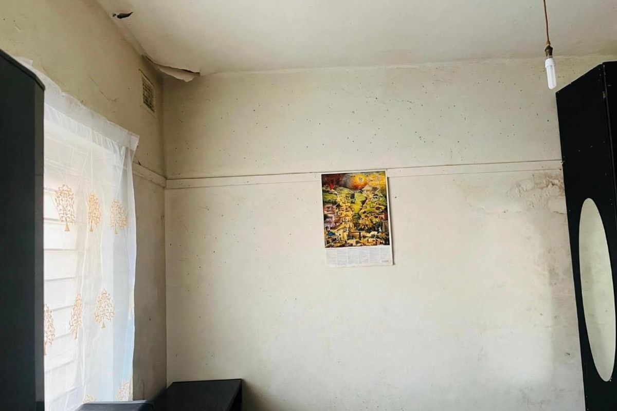 A bedroom interior showing signs of significant wear, including peeling ceiling paint and water damage on the walls, requiring maintenance and cosmetic updates.