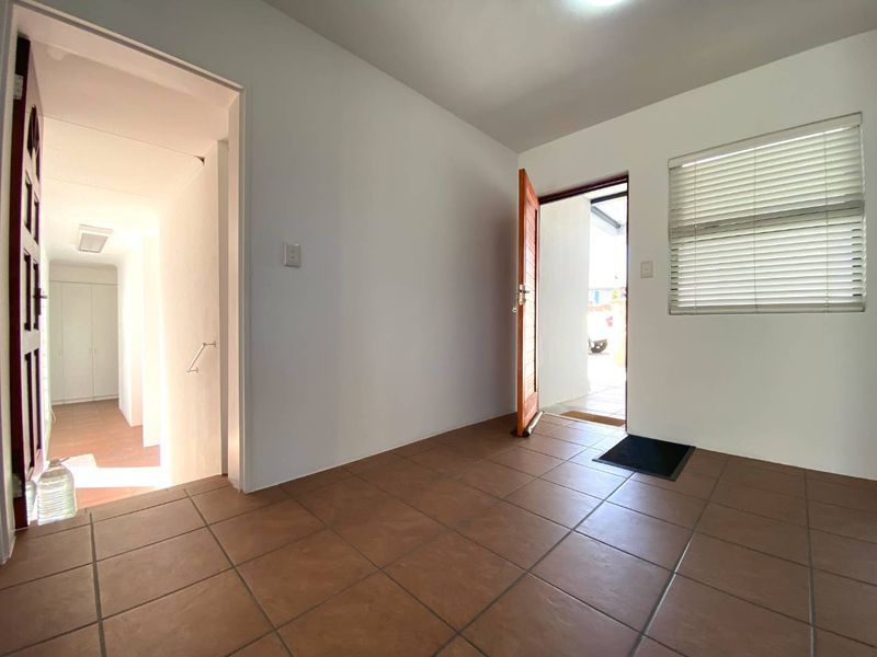 A bright and neutral entrance hall featuring tiled flooring, a timber door, and venetian blinds, leading into the interior living spaces.