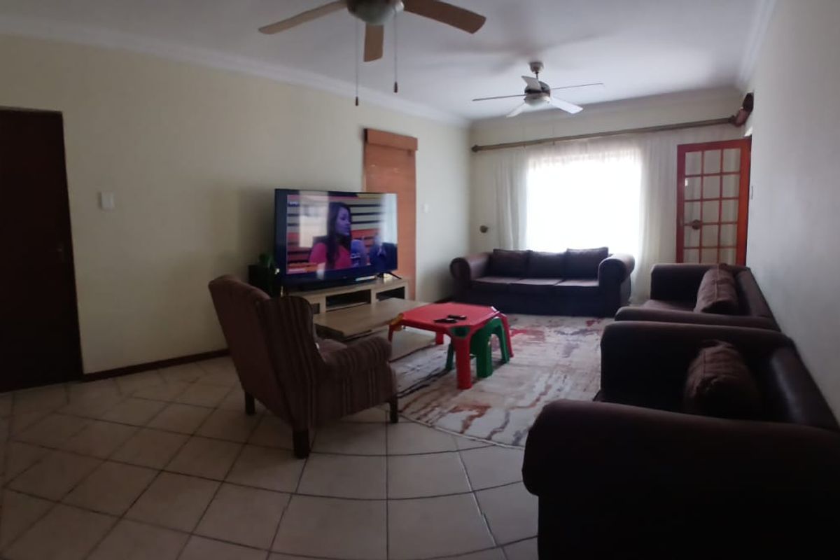 A spacious living room featuring tiled flooring, dual ceiling fans, and a large window allowing natural light into the area.