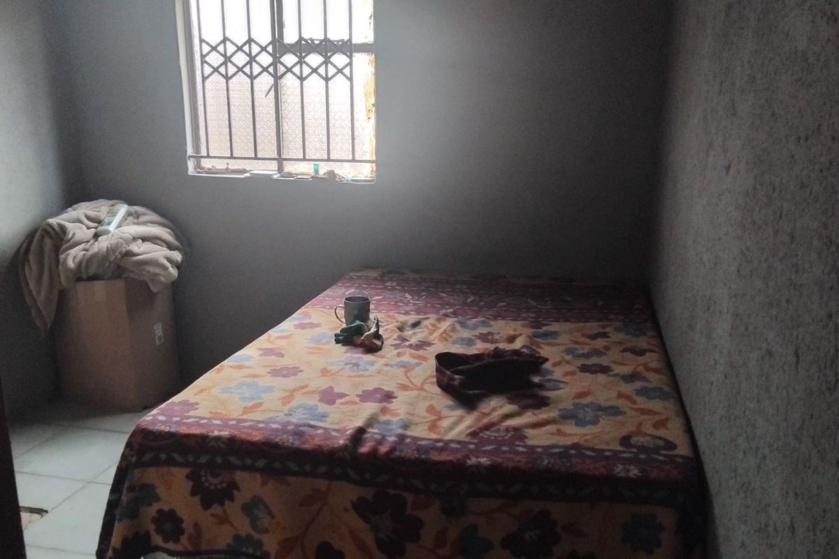 A compact bedroom featuring a window with a security gate and tiled flooring.