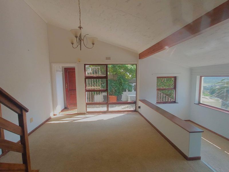 Spacious living area featuring vaulted ceilings with exposed timber beams, large windows providing natural light, and a timber staircase leading to another level.