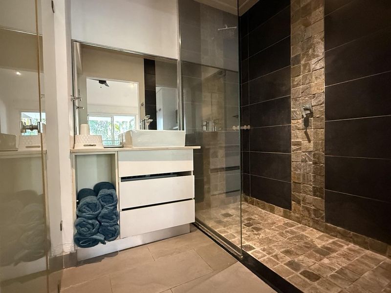 Modern bathroom featuring a sleek vanity with vessel sink, large wall mirror, and a spacious walk-in shower with stone tile accents and glass enclosure.