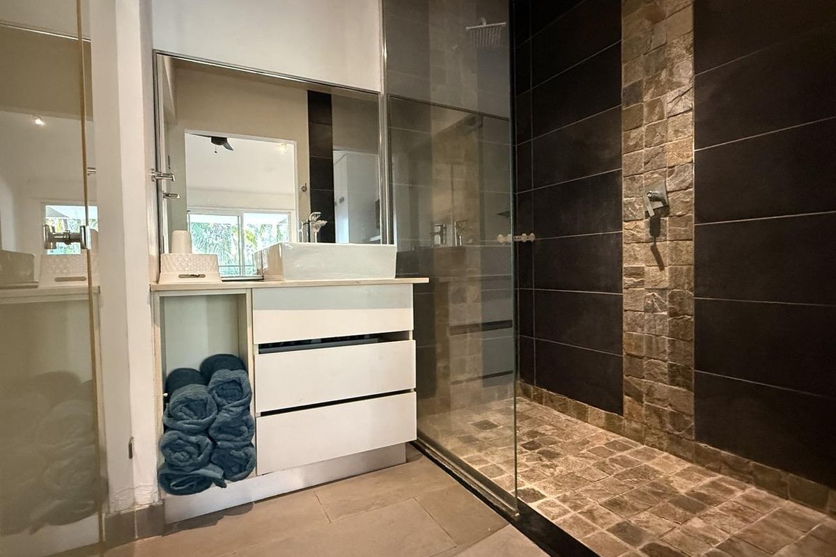 Modern bathroom featuring a sleek vanity with vessel sink, large wall mirror, and a spacious walk-in shower with stone tile accents and glass enclosure.