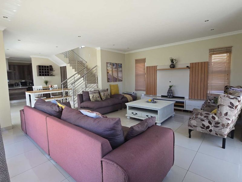 Spacious open-plan living area featuring tiled floors, a modern staircase with stainless steel balustrades, and a built-in media unit.